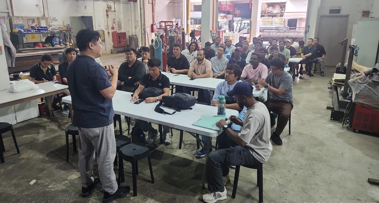 NC Contractor management presenting workplace safety briefing to construction workers at Tuas facility — Singapore safety culture in action
